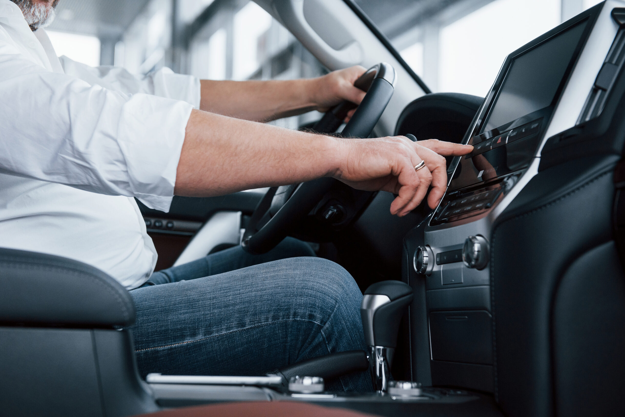 Side close up view. Businessman in official clothes sits in a luxury car and pushing the buttons on the music player.